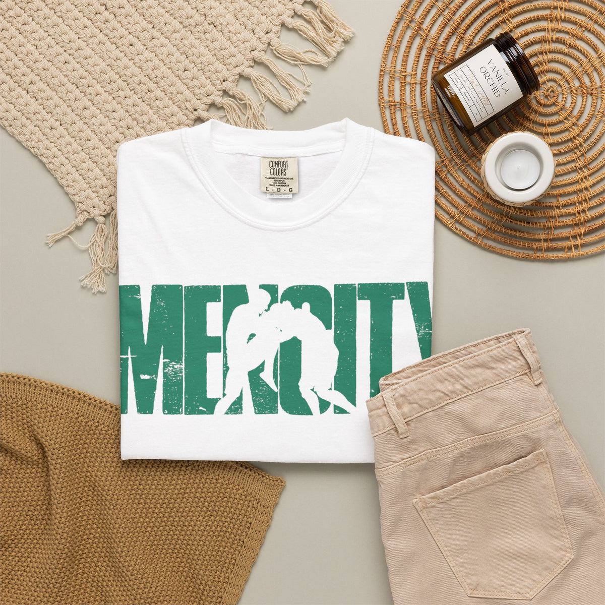 White Mencity Fighter gym t-shirt folded in a flat lay with beige trousers and a candle