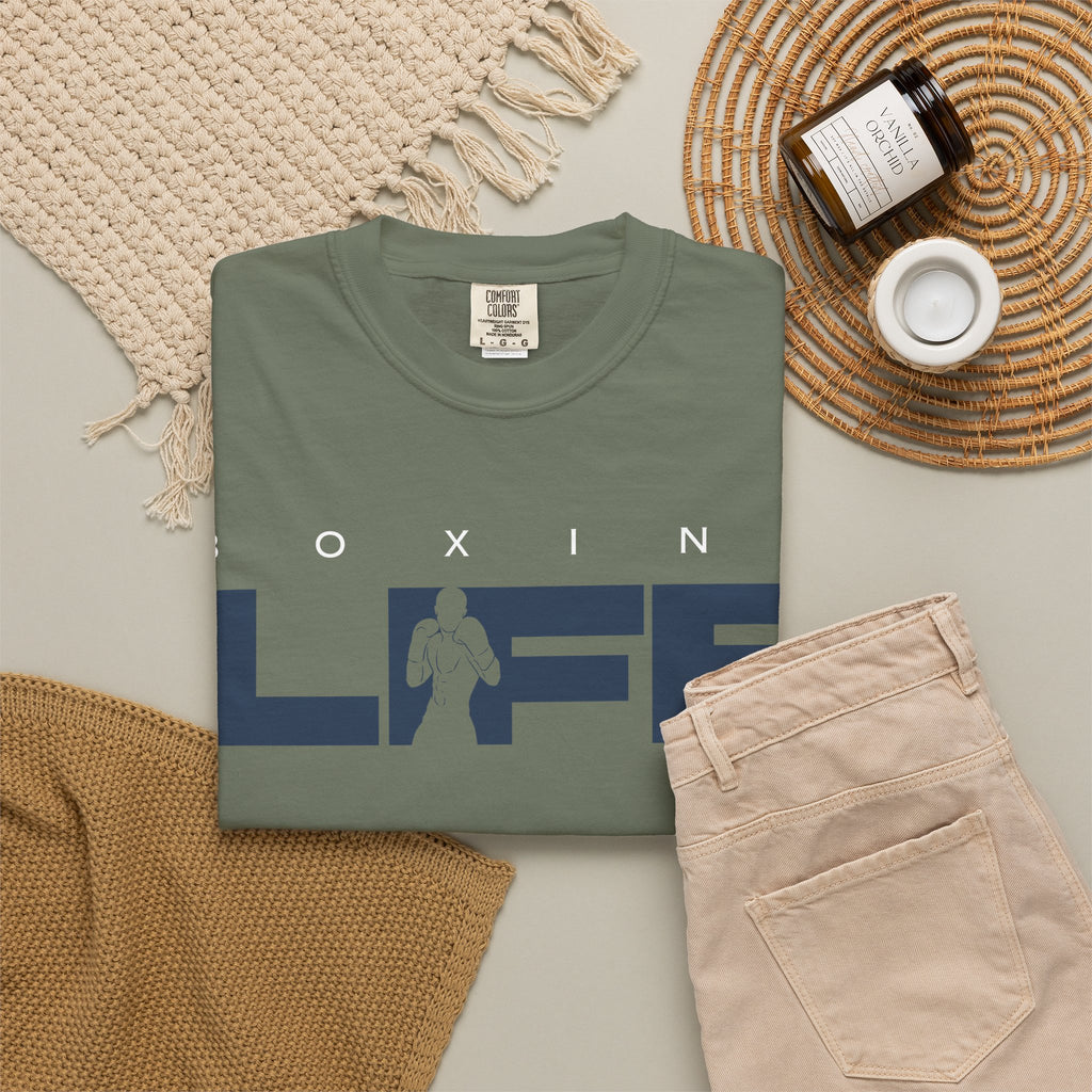 Moss green Mencity Boxing Life t-shirt folded in a flat lay with beige trousers and a candle