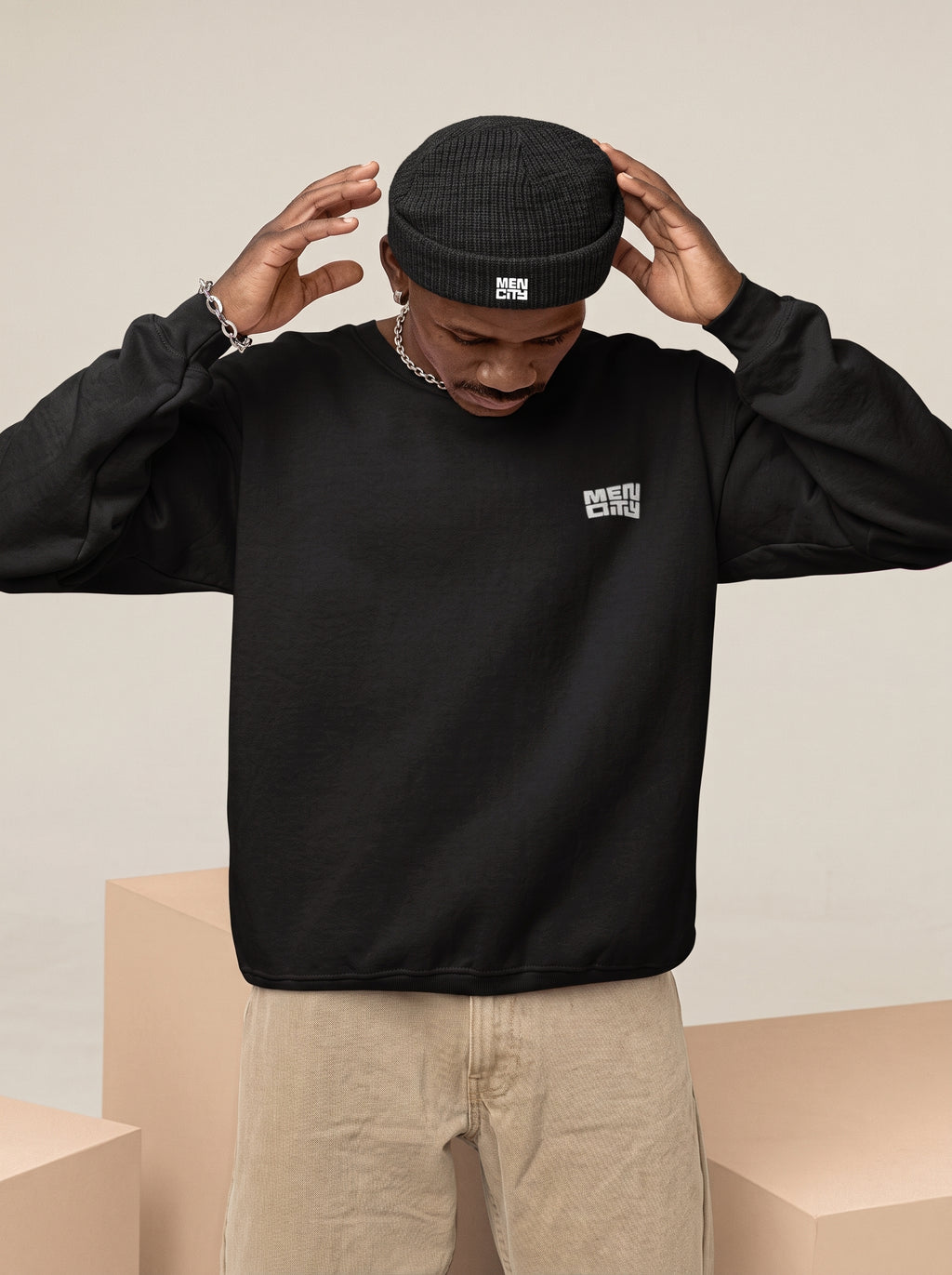 Man in a black sweatshirt adjusting a black Mencity cuffed beanie with the embroidered logo, front view