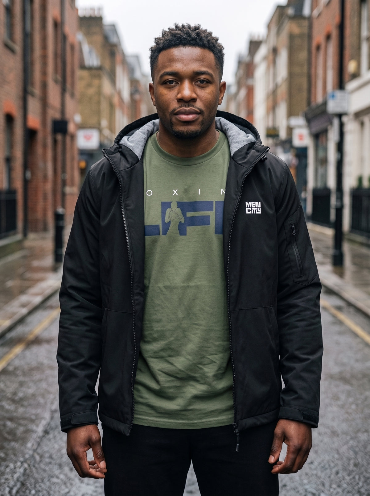 Man in a black Mencity waterproof insulated jacket over a green Boxing Life tee, standing on a London street